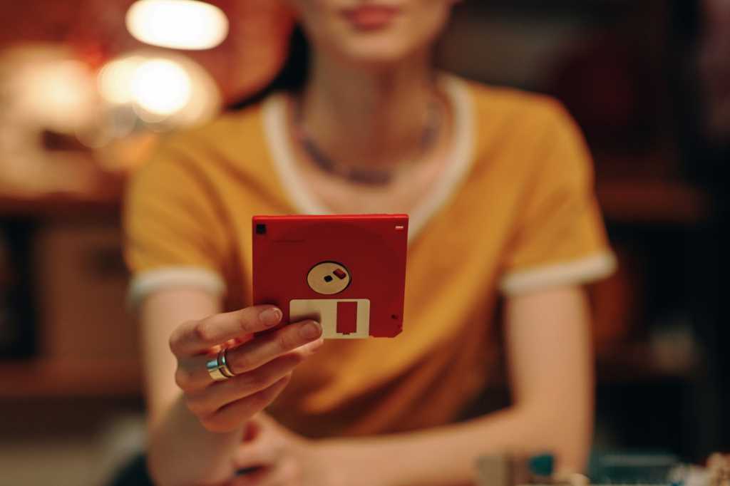 Woman in yellow holding up a red floppy disk at her desk